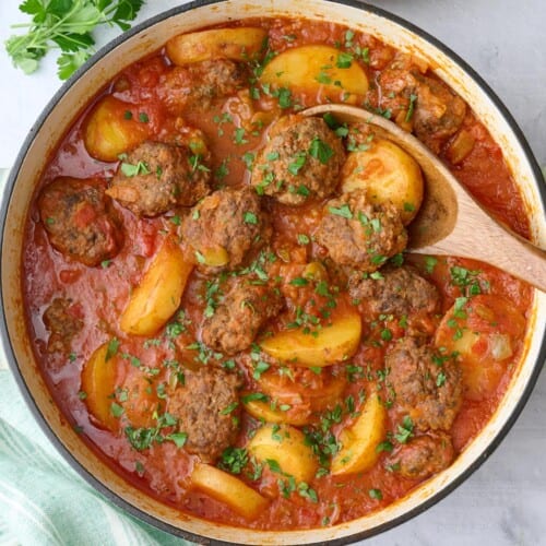 Kafta Potato Stew in the pot garnished lightly with chopped parsley, serving spoon, small dish of chopped parsley, and serving dish of Lebanese rice nearby.