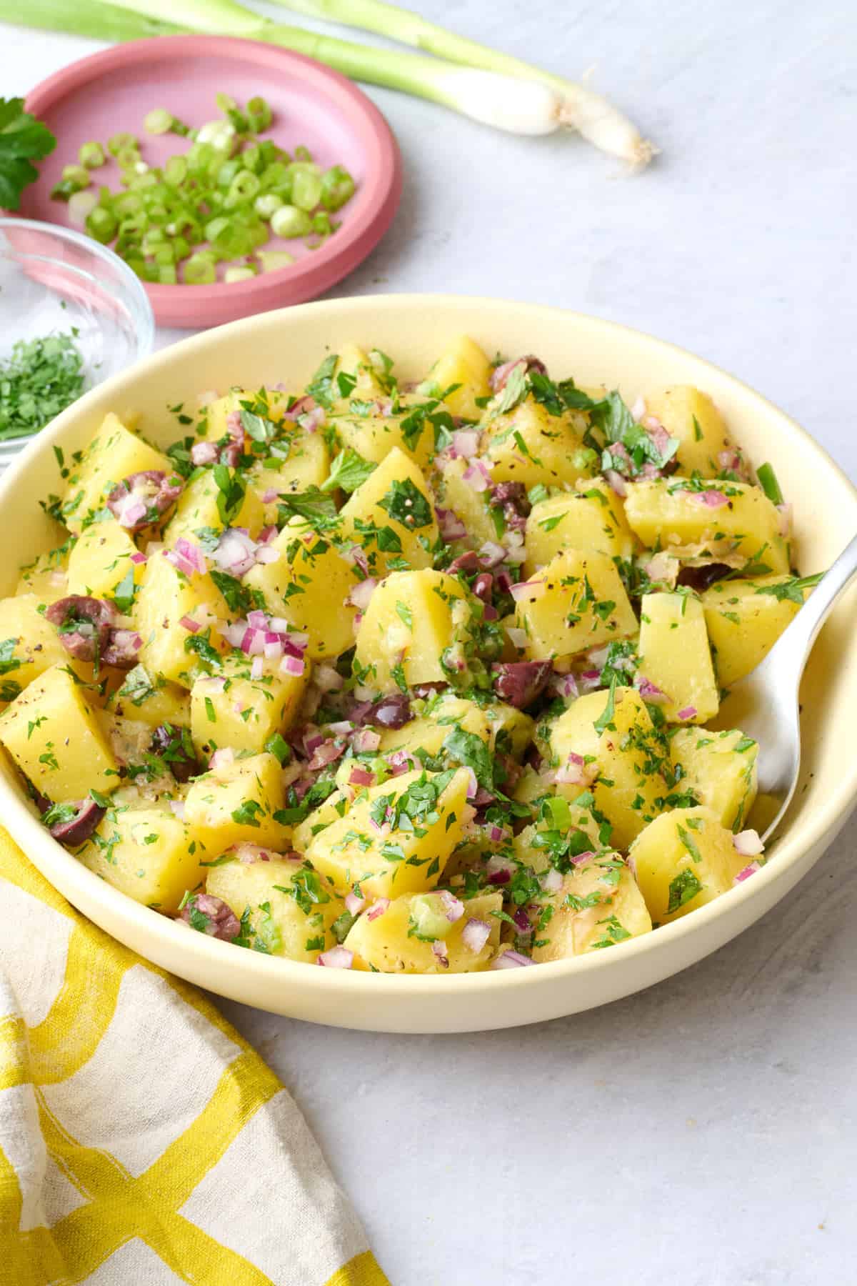 Potato salad in a serving bowl with parsley on top and extra ingredients around.