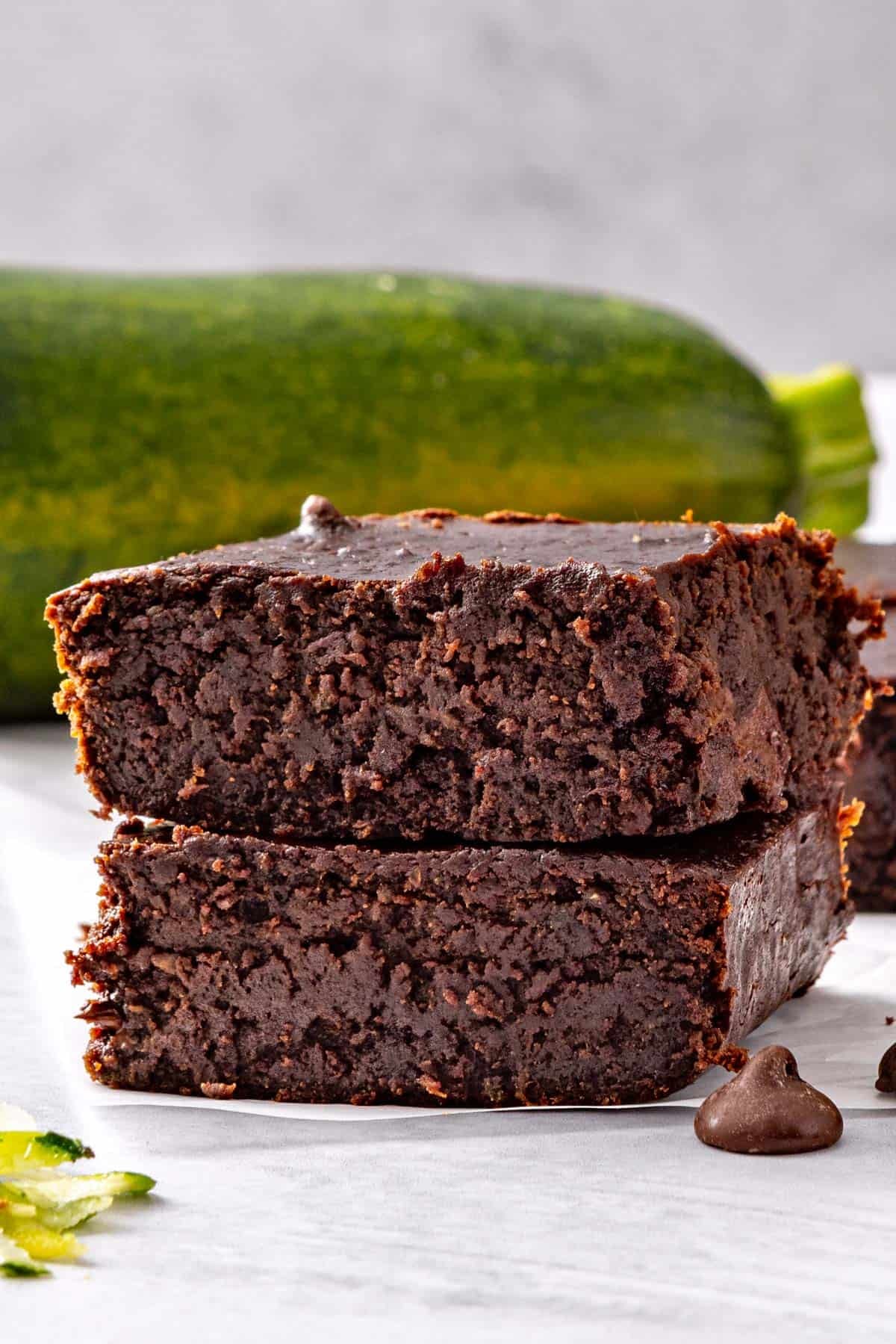 Two brownies stacked on top of each other with a zucchini in the back.