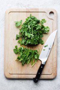 cilantro with ends cut off on a wooden chopping board