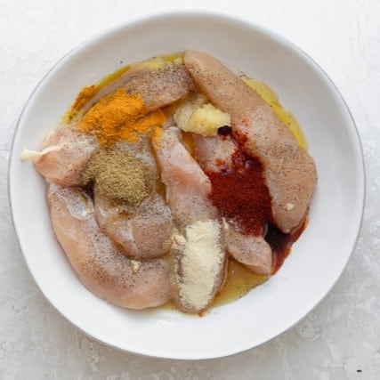 Chicken with seasonings in a bowl before mixing.