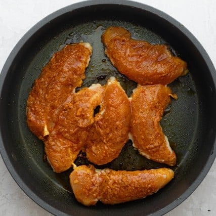 Raw, seasoned chicken in a skillet before cooking.