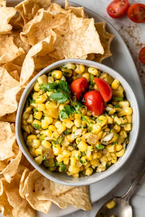 Close up shot of bowl of corn salsa with chips around the bowl