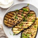 Grilled eggplant on a plate topped with pinenuts