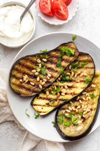 Grilled eggplant on a plate topped with pinenuts