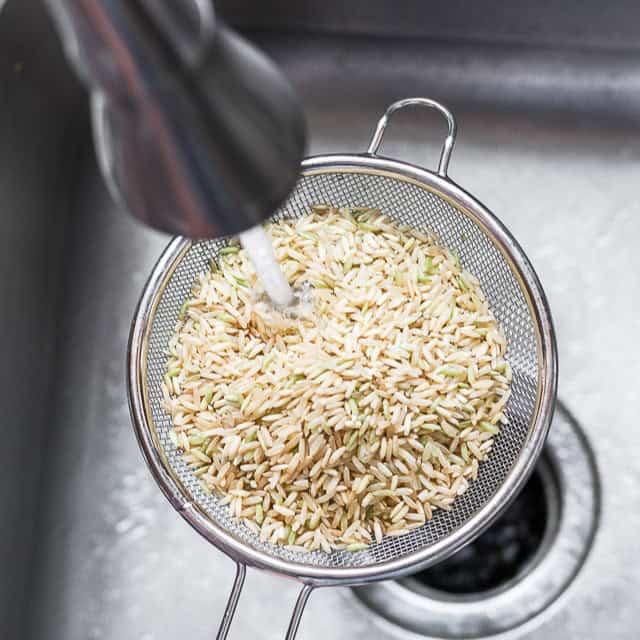 Brown rice in a fish mesh sieve under a faucet.
