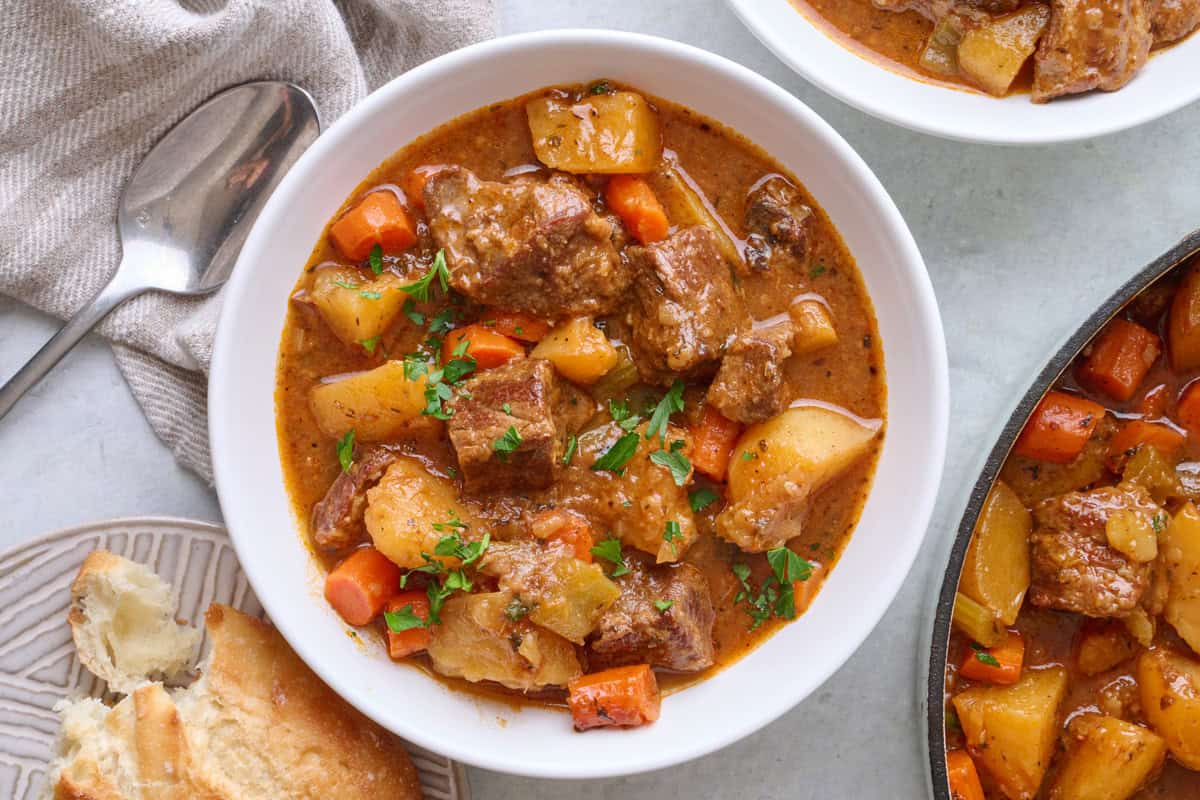 Stovetop beef stew in a bowl with a pot filled with more nearby.