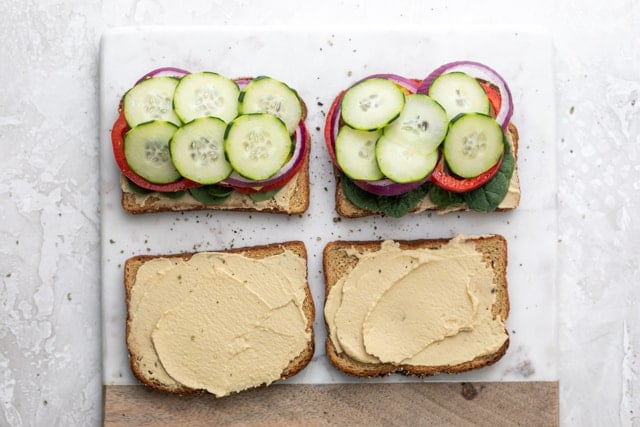 Adding final layer of cucumbers on top of the hummus