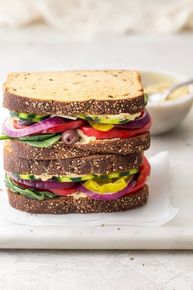 Veggie and hummus sandwiches stacked on top of each other with small bowl of hummus in background