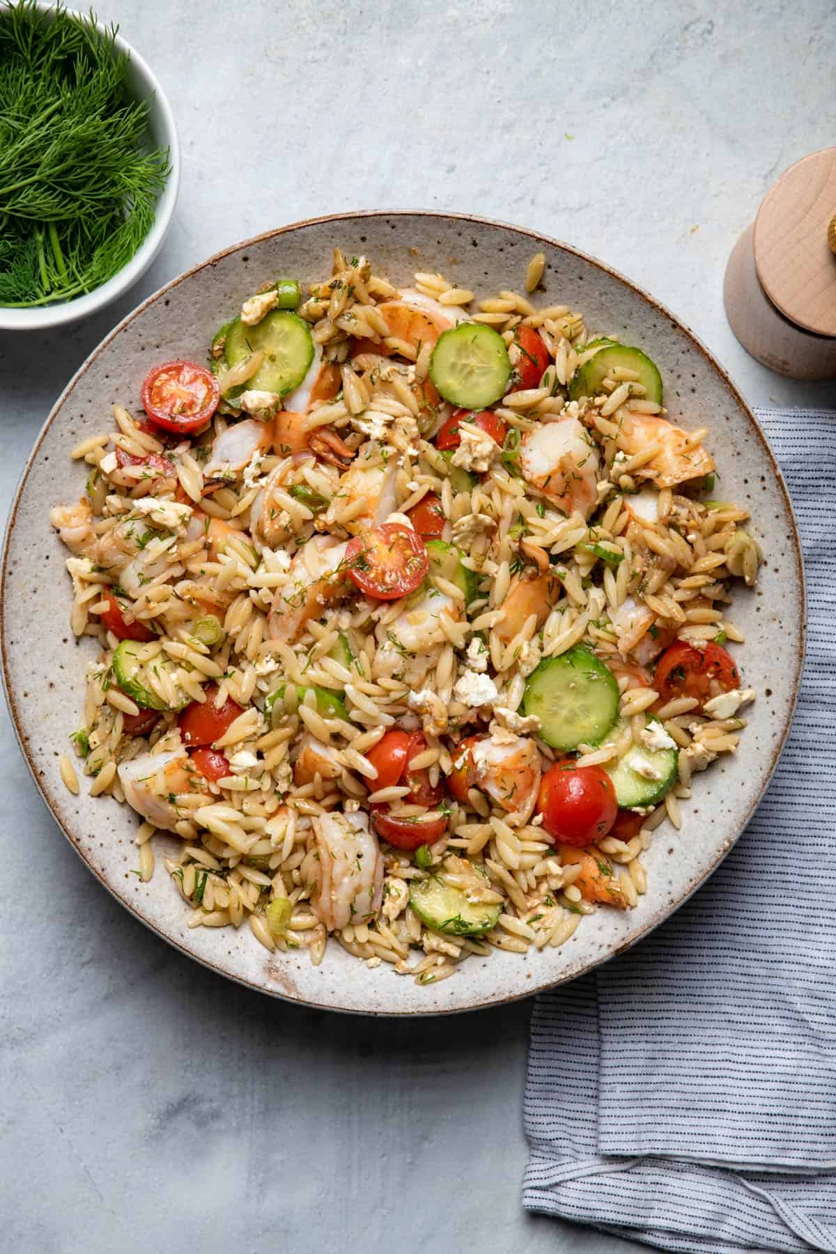 Large serving bowl of shrimp orzo salad with dill on the side