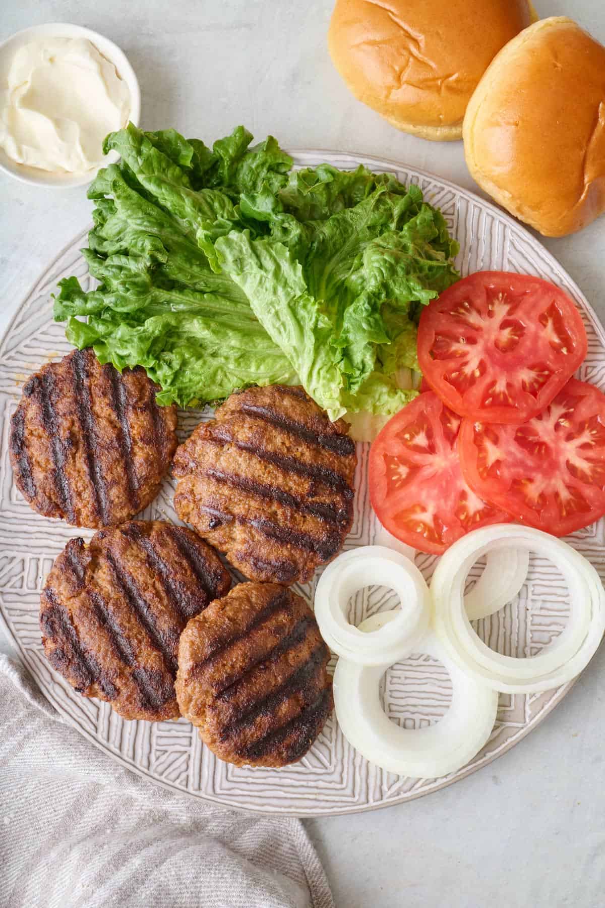 Platter of grilled hamburger patties, lettuce, sliced tomatoes, and onions.