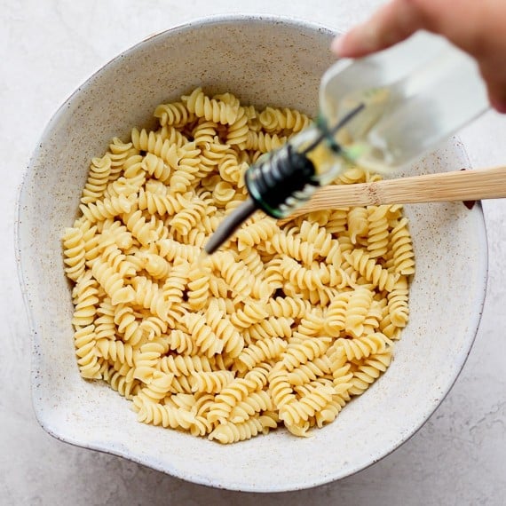 Olive oil being drizzled over cooked pasta.
