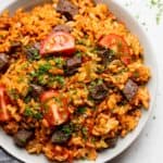 Jollof rice served in a bowl with beef and tomatoes on top