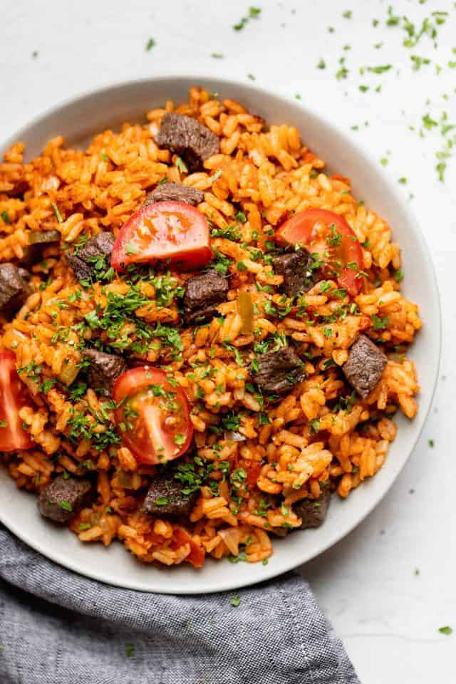 Jollof rice served in a bowl with beef and tomatoes on top