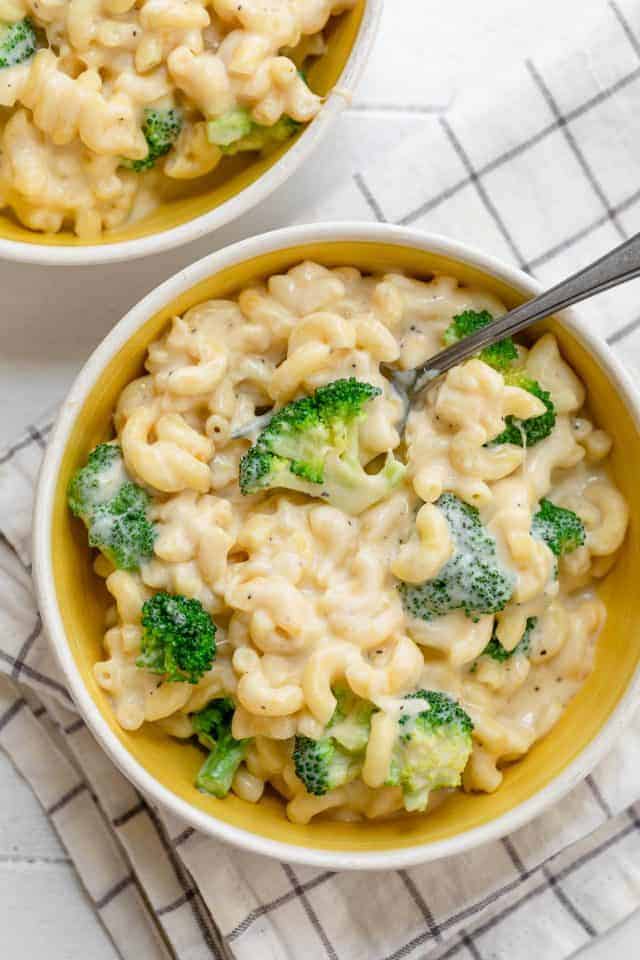 Large bowl of broccoli mac and cheese with spoon inside and second bowl nearby