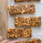 Hand grabbing one of the caramel apple granola bars on board with parchment paper