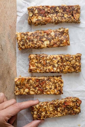 Hand grabbing one of the caramel apple granola bars on board with parchment paper