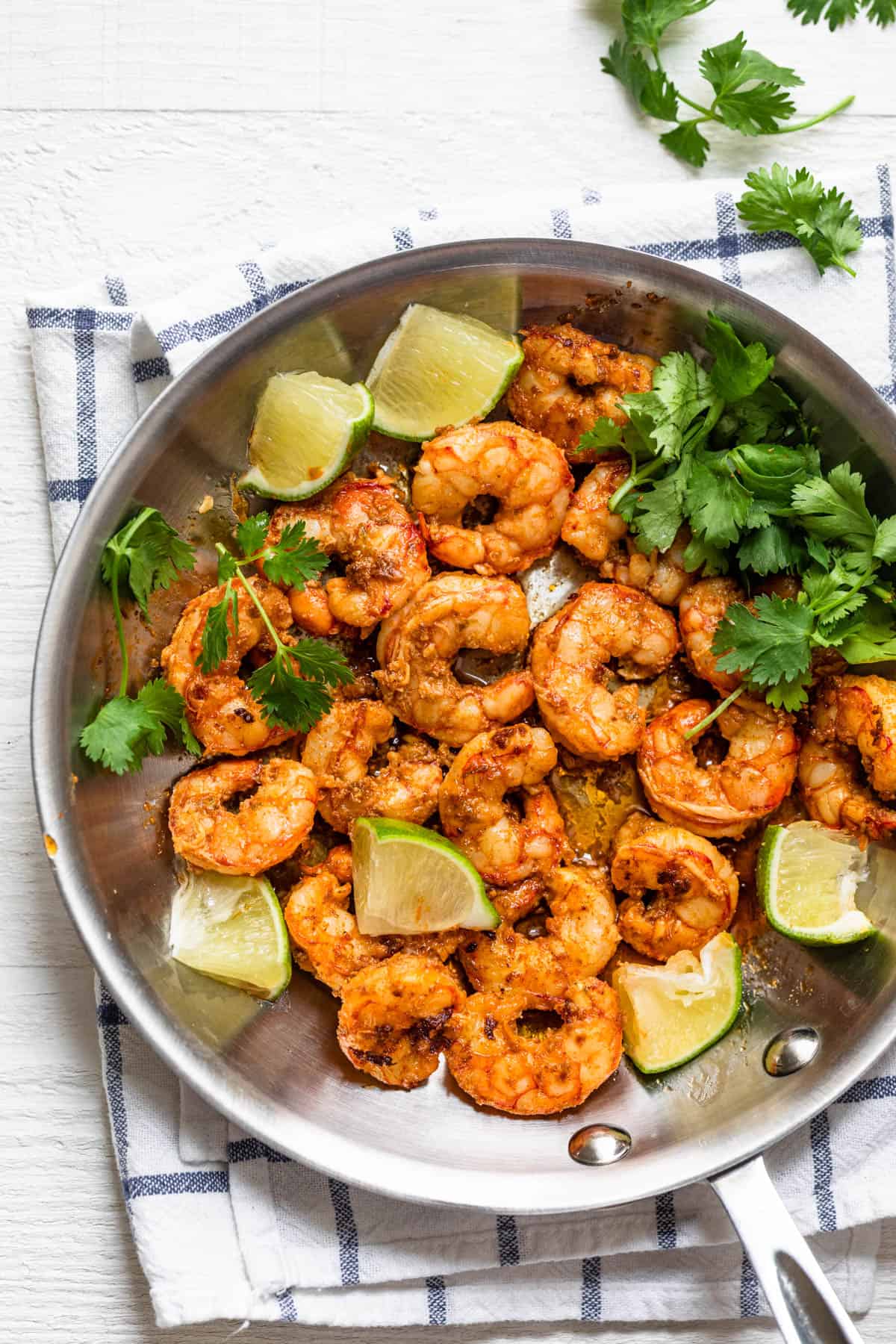 Chili lime shrimp in a saute pan with cilantro and lime wedges