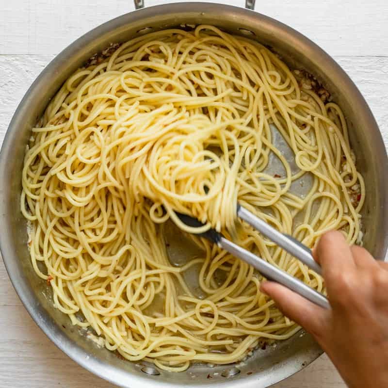 Tongs mixing the pasta with the garlic butter.