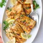 Grilled mahi mahi fillets on a large platter garnished with chopped parsley and lemon wedges, small bowl of mango salsa nearby.