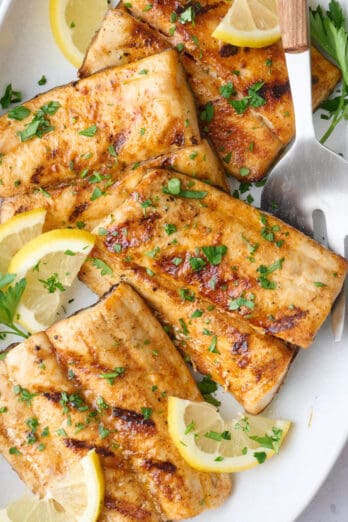 Grilled mahi mahi fillets on a large platter garnished with chopped parsley and lemon wedges, small bowl of mango salsa nearby.
