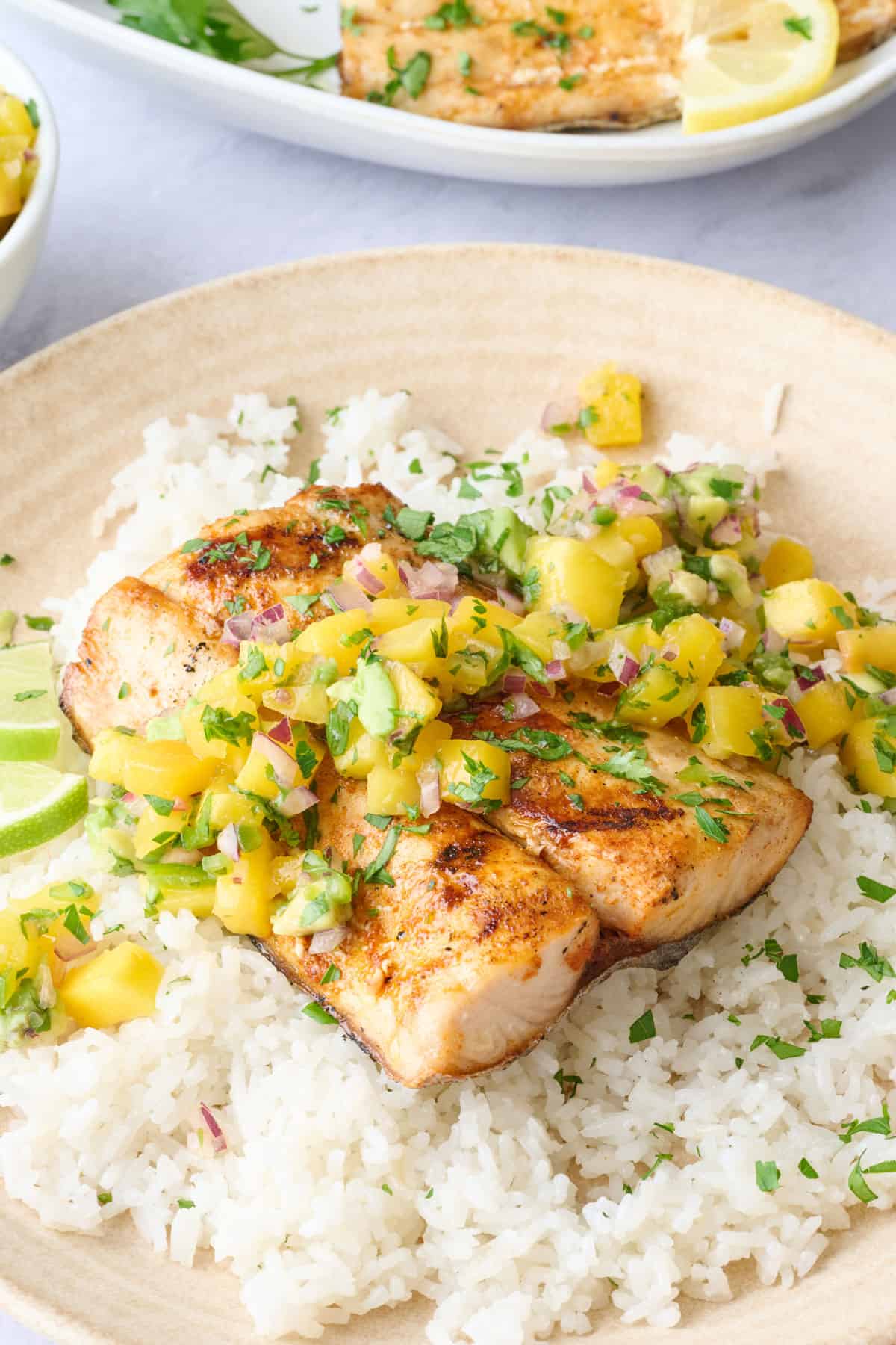 Serving of mahi mahi on a plate with coconut rice and mango salsa spooned lightly on top.