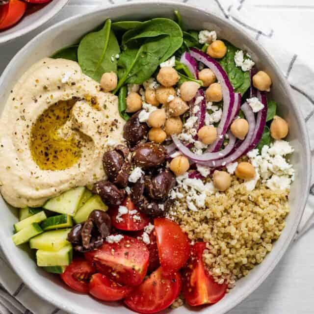 Close up of large full hummus bowl with cucumbers, tomatoes, quinoa, chickpeas, spinach, onions and feta cheese