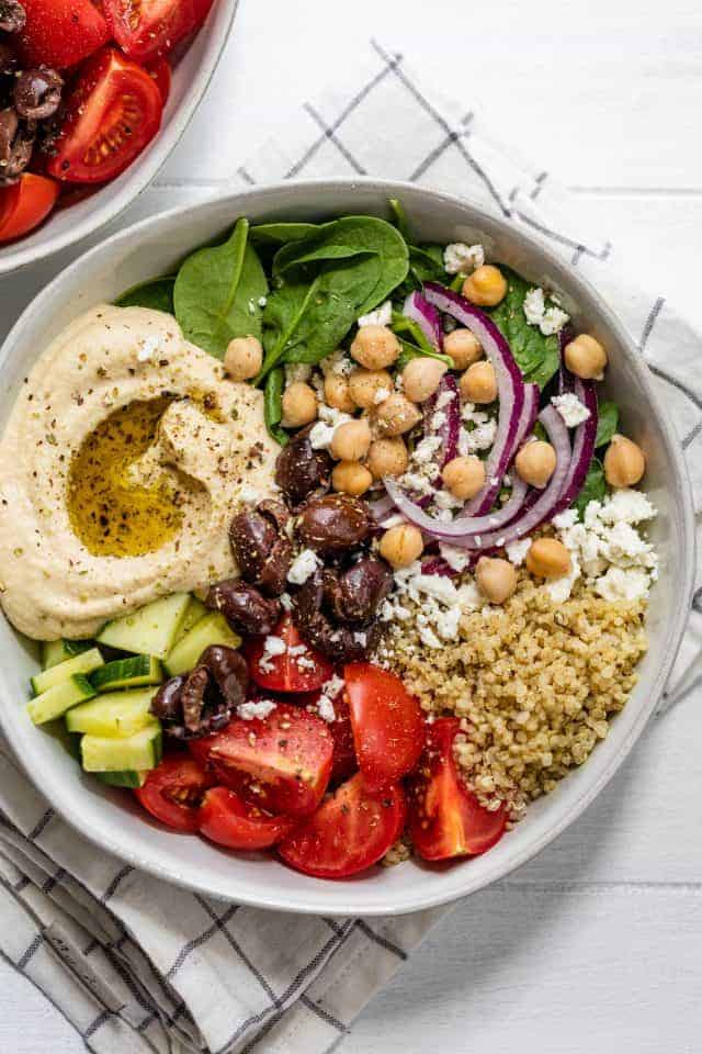 Close up of large full hummus bowl with cucumbers, tomatoes, quinoa, chickpeas, spinach, onions and feta cheese