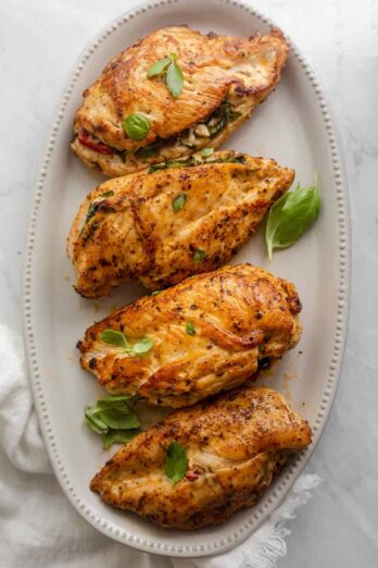 Mediterranean stuffed chicken on a long serving plate garnished with basil