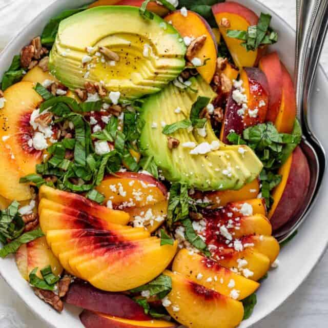 Large bowl of summer peach salad with spinach and avocado with large serving spoon inside