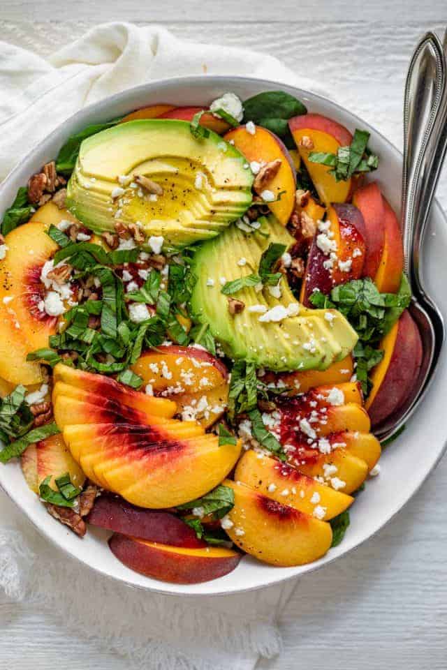 Large bowl of summer peach salad with spinach and avocado with large serving spoon inside