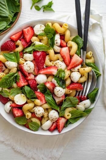 Strawberry caprese salad in large bowl with serving utensils in bowl