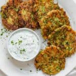 Zucchini fritters on a white plate with labneh dipping sauce