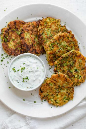 Zucchini fritters on a white plate with labneh dipping sauce