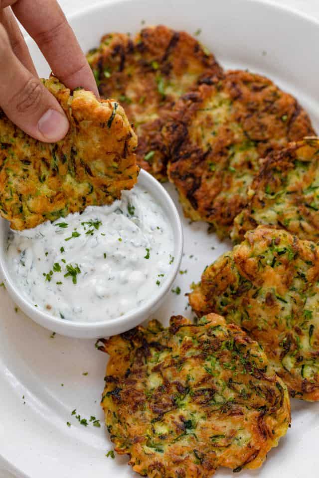 Hand holding zucchini fritters dipping into labneh cilantro sauce