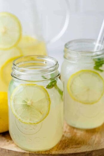 Homemade lemonade in a cup with glass jug in the background and lemons on the side