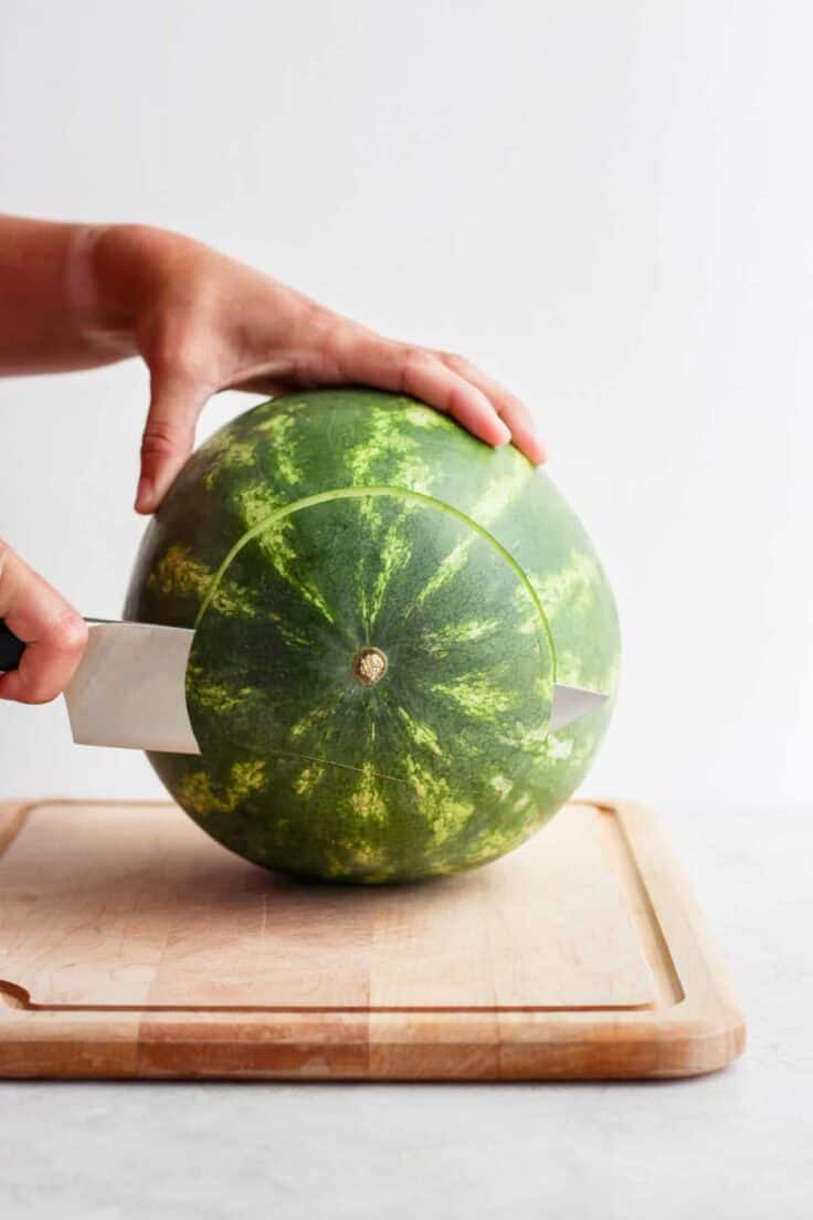 Large watermelon on cutting board with bottom part getting cut off