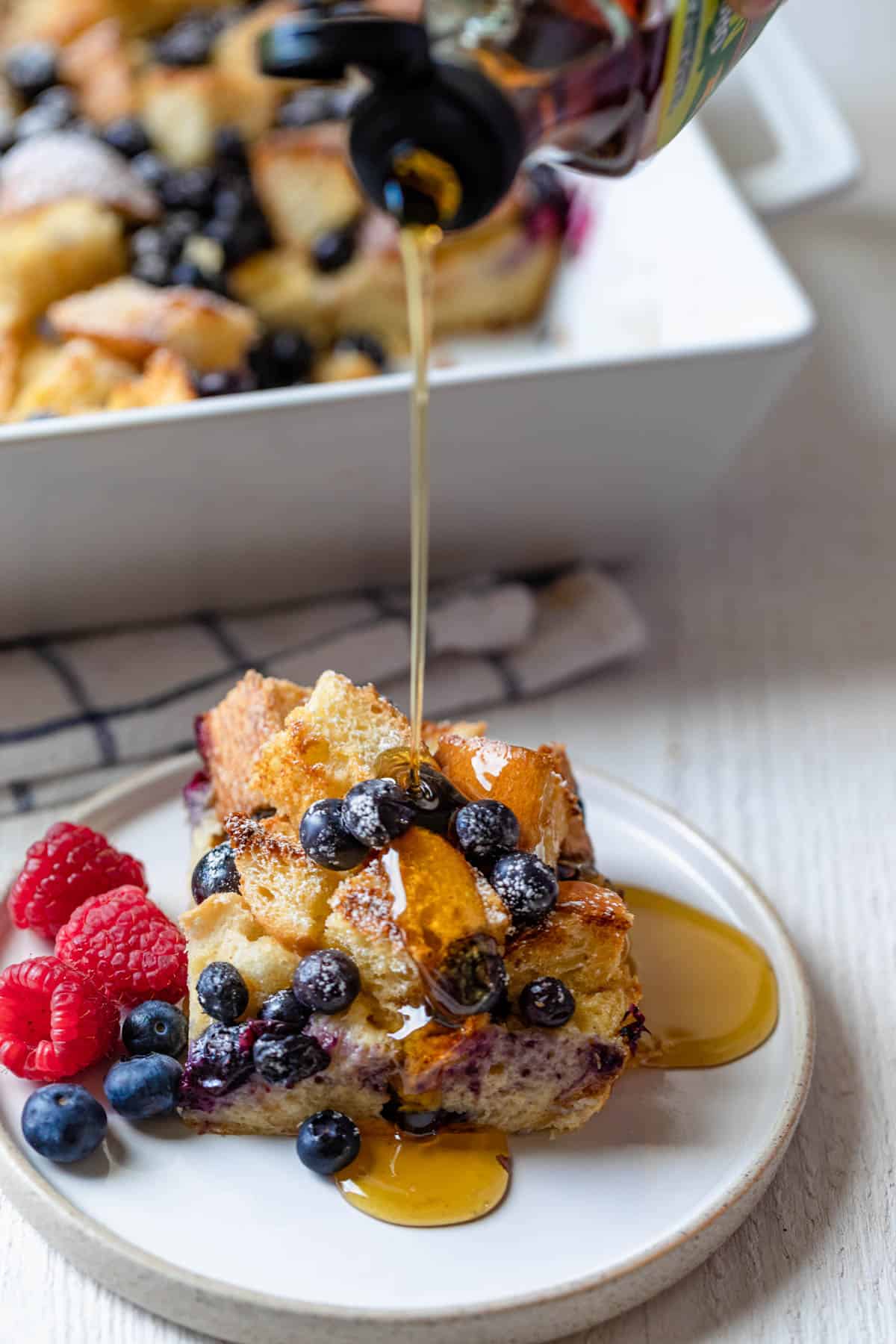 Maple syrup drizzling over slice of blueberry french toast casserole