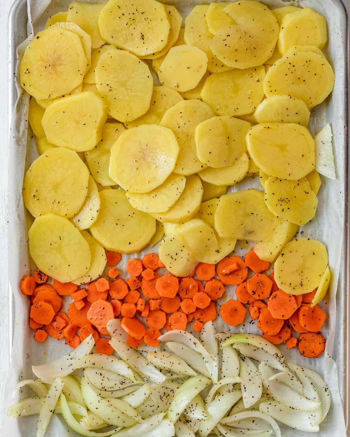 Potatoes, carrots, and onions on a baking sheet.