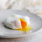 A poached egg broken so the yolk is coming out, on a plate.