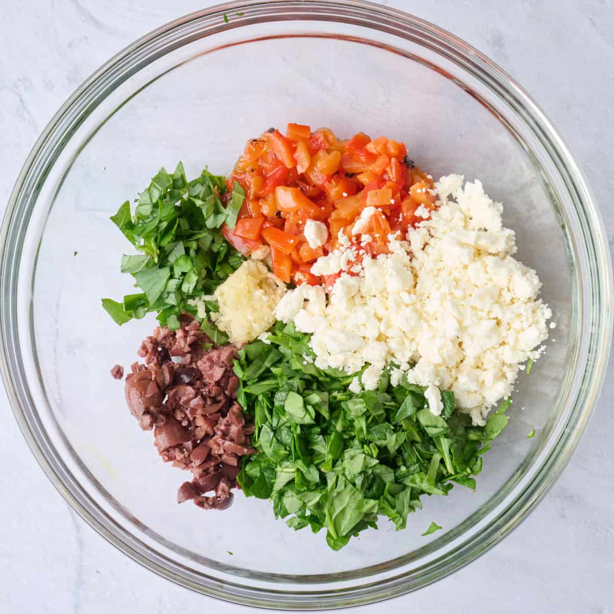 Spinach, feta, roasted red peppers, olives, basil, garlic, and oil in a bowl before combining.