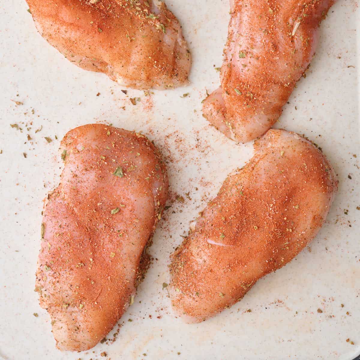 Cut chicken breasts seasoned with oregano, paprika, salt and pepper on a cutting board.