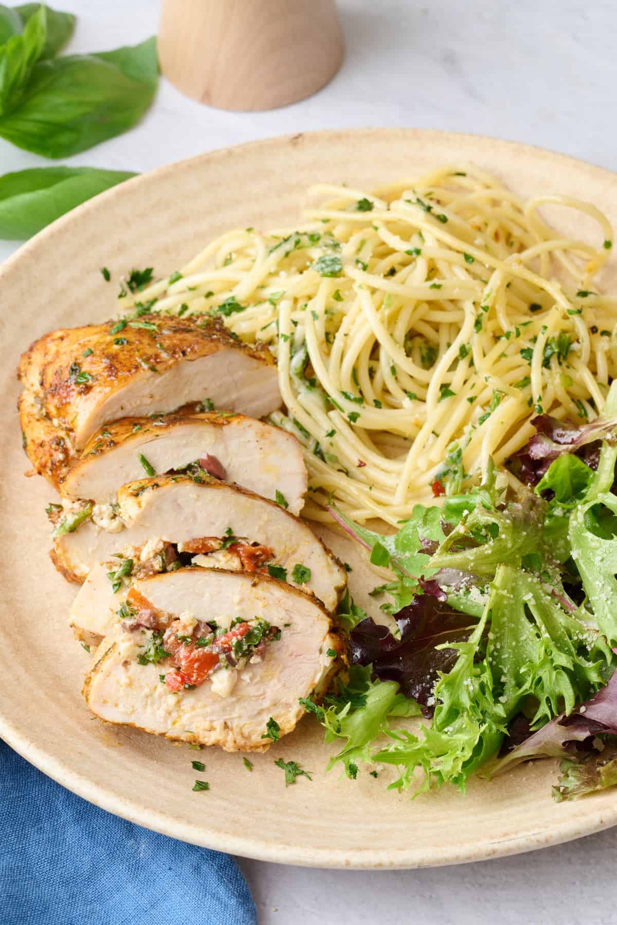 1 stuffed chicken breast on a plate with pasta and spring mix salad with a piece cut away to show filling.