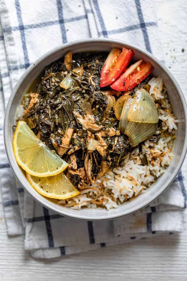 Large bowl of molokhia topped with shredded chicken, tomatoes and lemon slices and served over rice