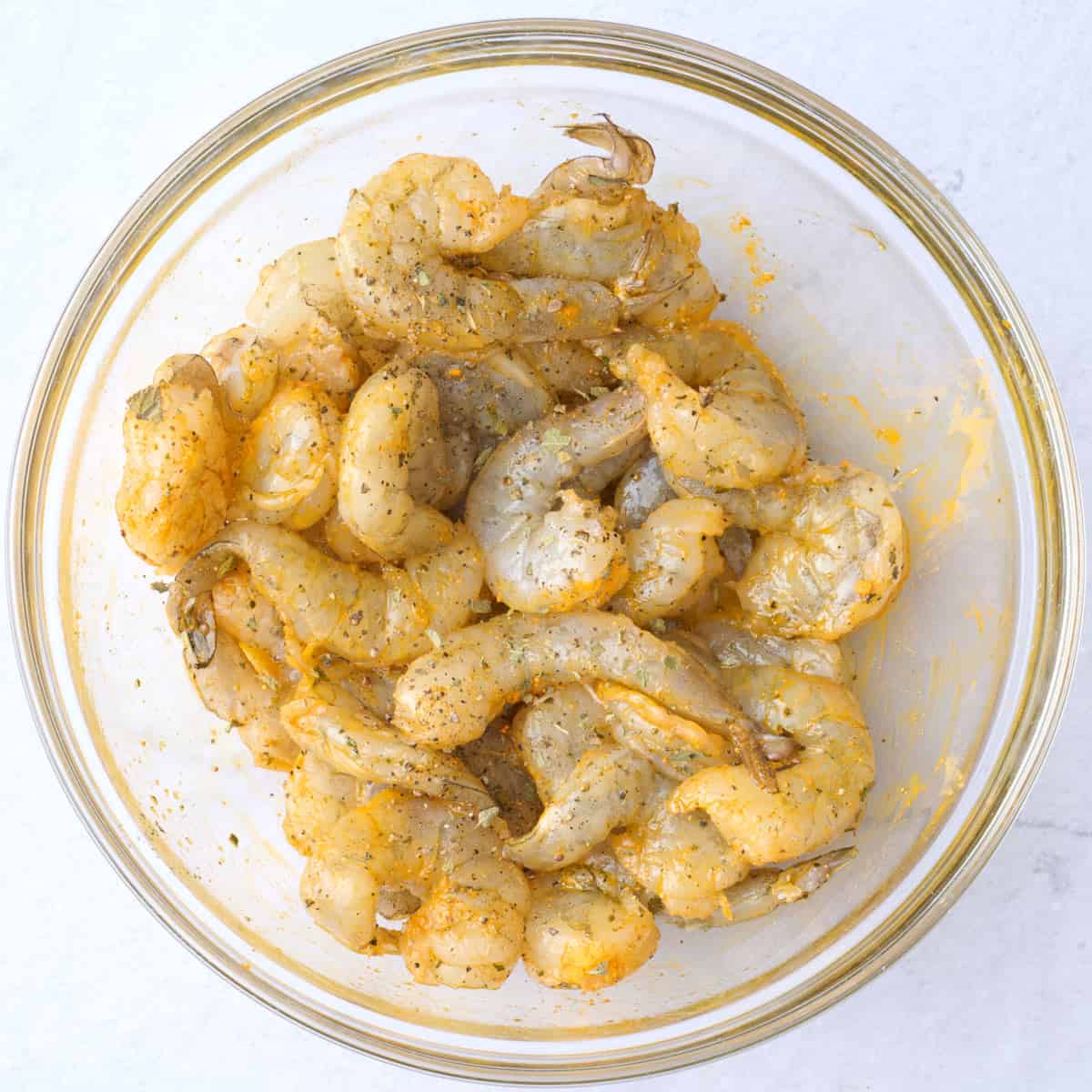 Shrimp in a small bowl tossed with oil, oregano, turmeric, salt and pepper.