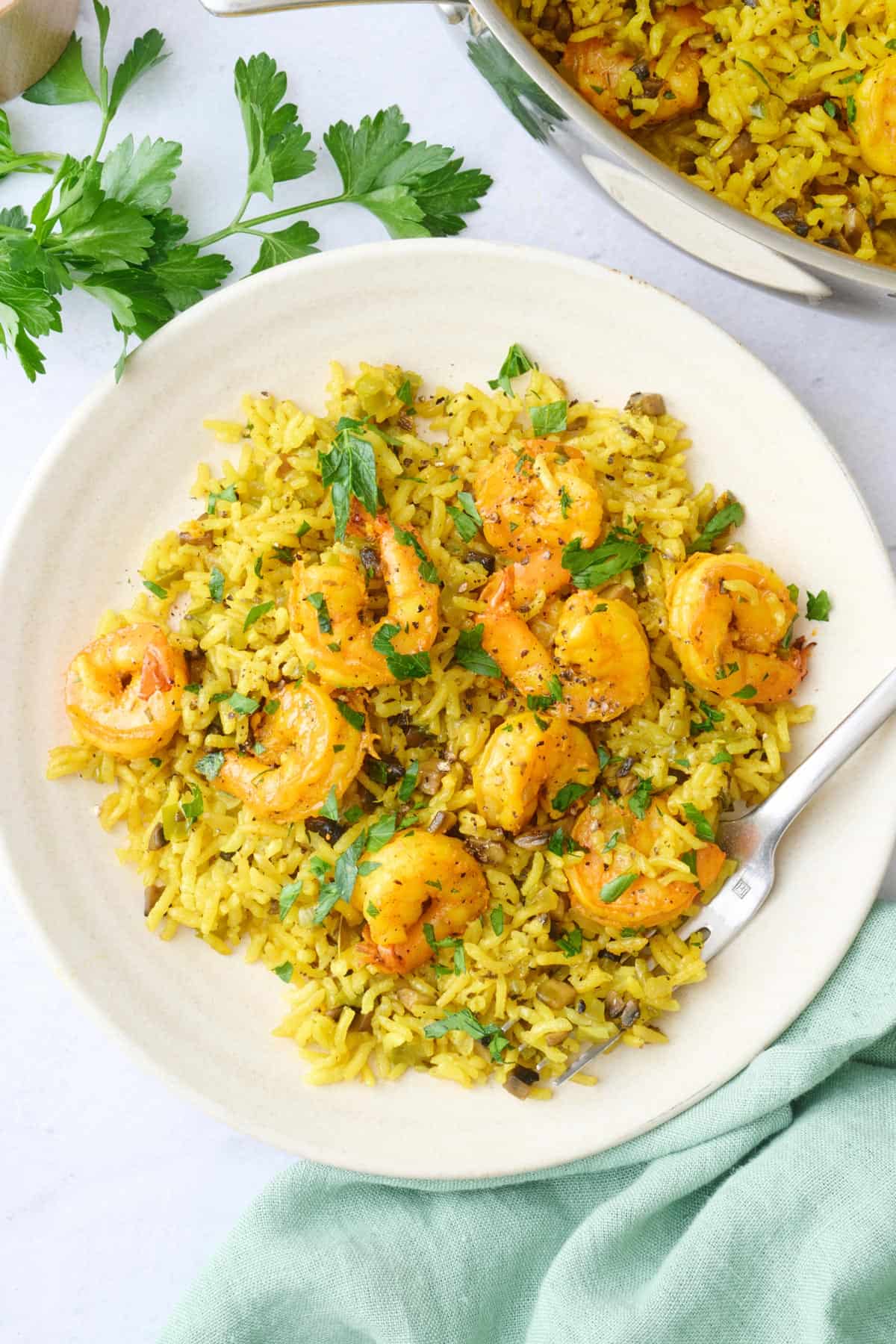 A serving of shrimp and rice on a small plate with the pot nearby.