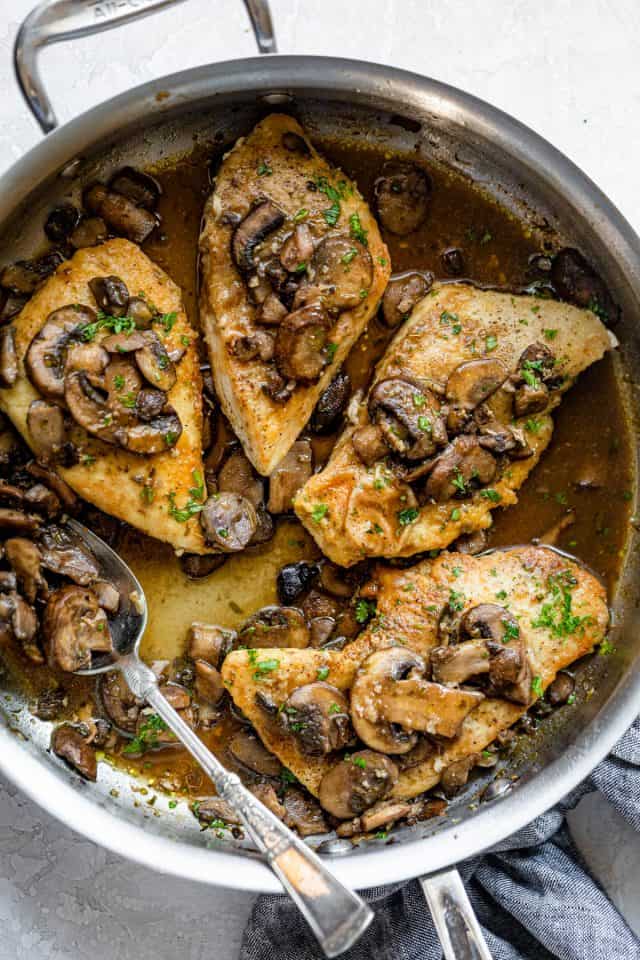 Sauteed chicken and mushrooms in a skillet with spoon inside for the sauce