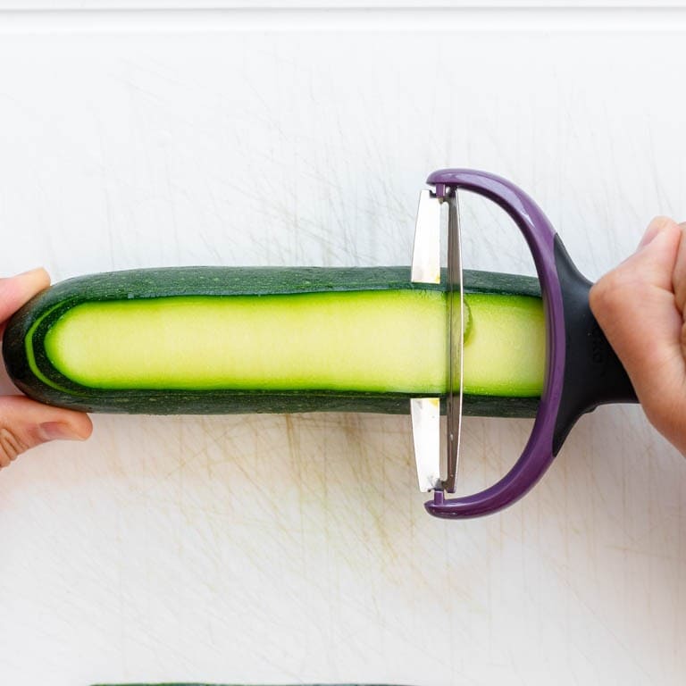 Peeling a zucchini with a wide peeler from left to right.
