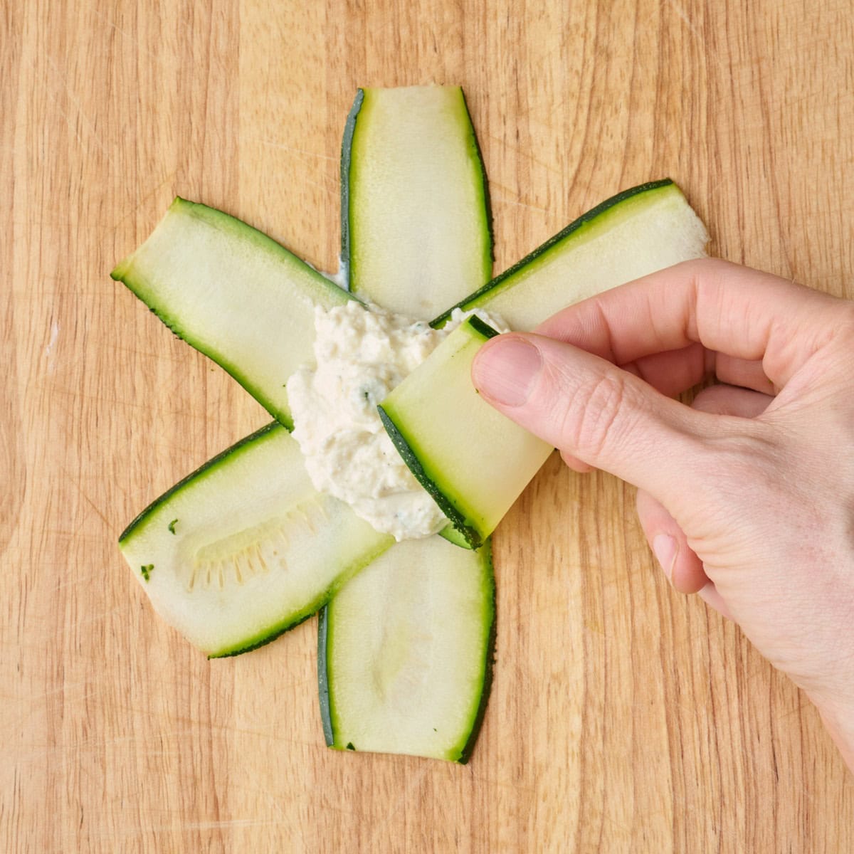 Folding up one piece of zucchini to reach the middle.