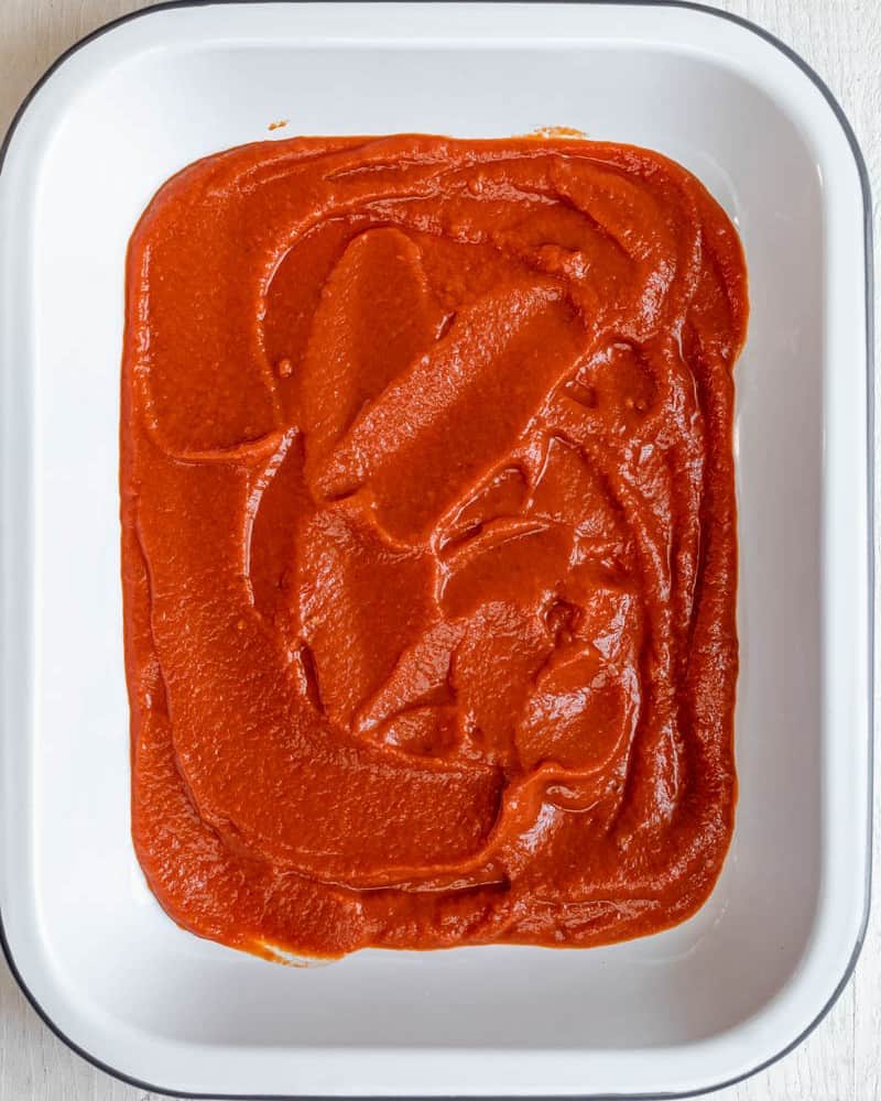 The baking dish fully covered in tomato sauce, before adding any zucchini ravioli on top.